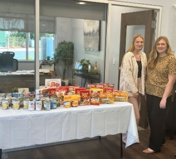 Employees smiling next to table of food donations.