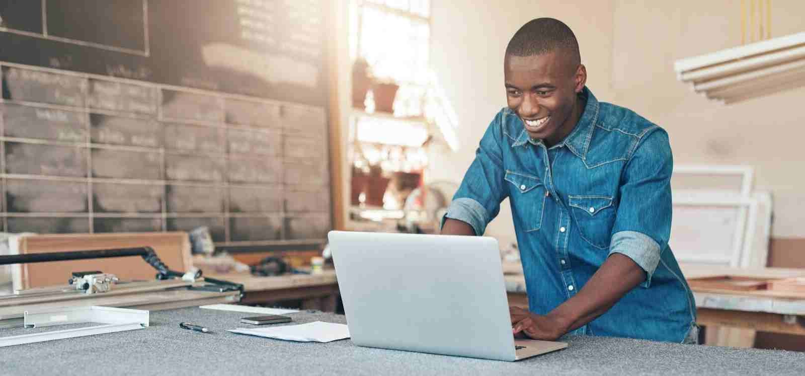 Man in a workshop looking at a laptop and smiling