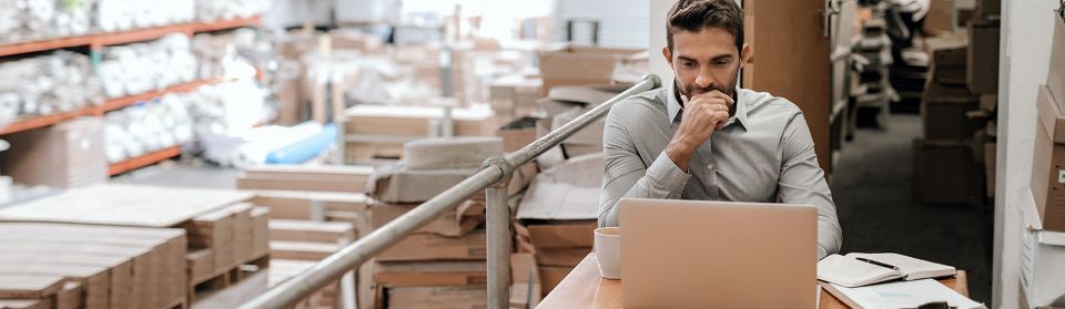 Man working on his laptop in a shipping warehouse full of boxes