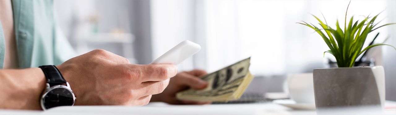 Closeup of hand holding phone and cash.