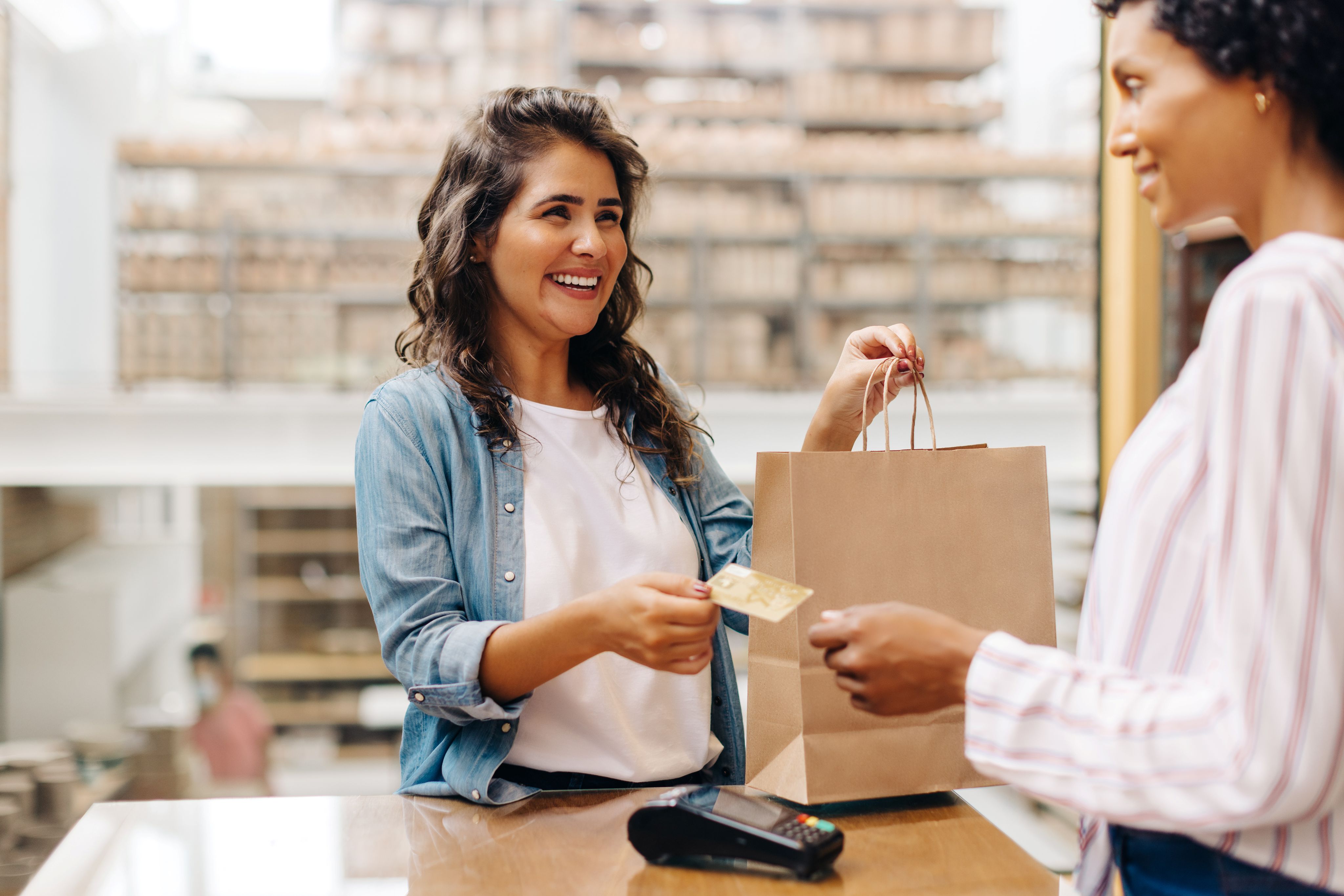 Female business owner handing bag and debit card to female customer while smiling.