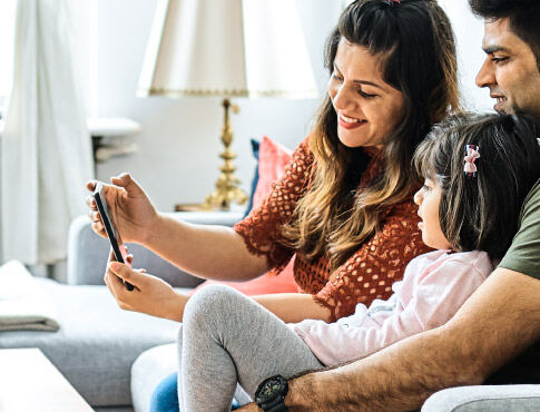 Family sitting on the couch in the living room while looking at a mobile phone.