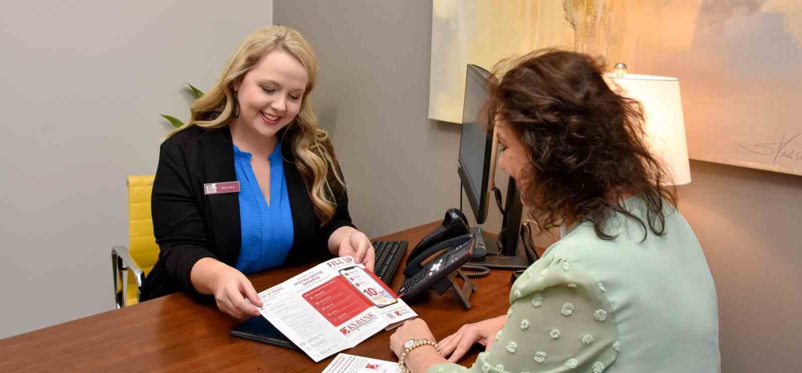 two women sitting across from each other looking over a brochure