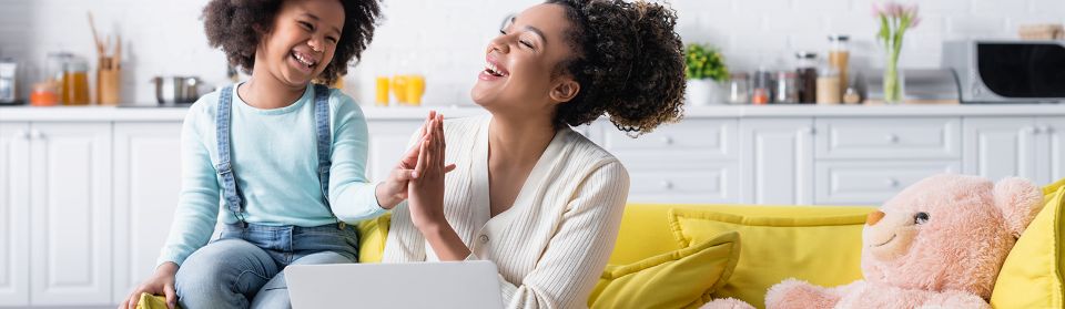 Young mother giving high five to young daughter on couch.