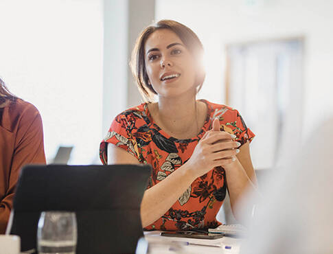 Woman smiling in meeting with hands clasped.