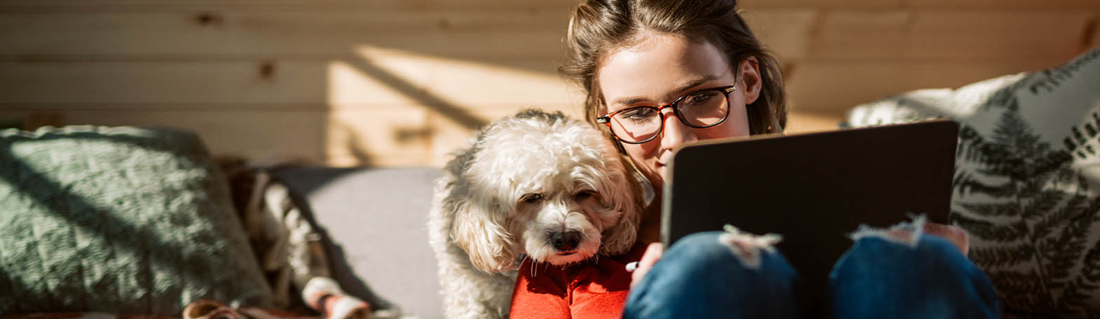 Woman holding laptop sits next to dog on couch.
