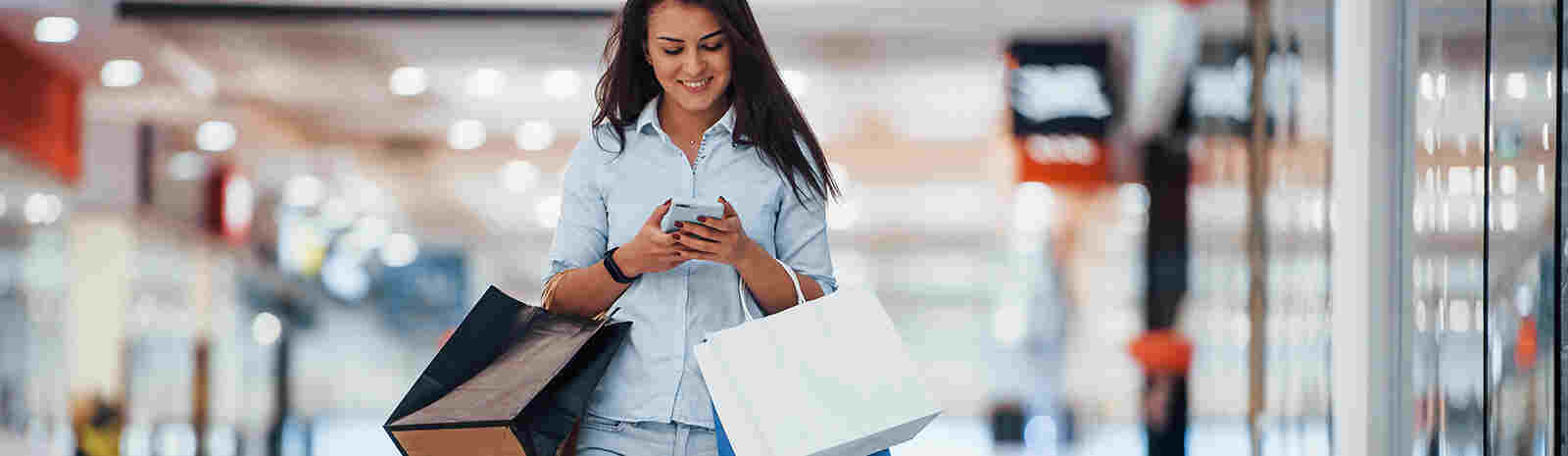 woman walking in mall with shopping bags while looking at phone