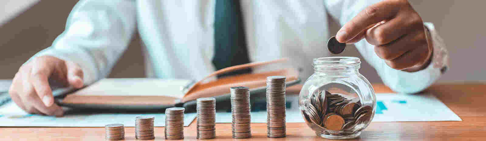 Closeup of man stacking money and putting change into jar.