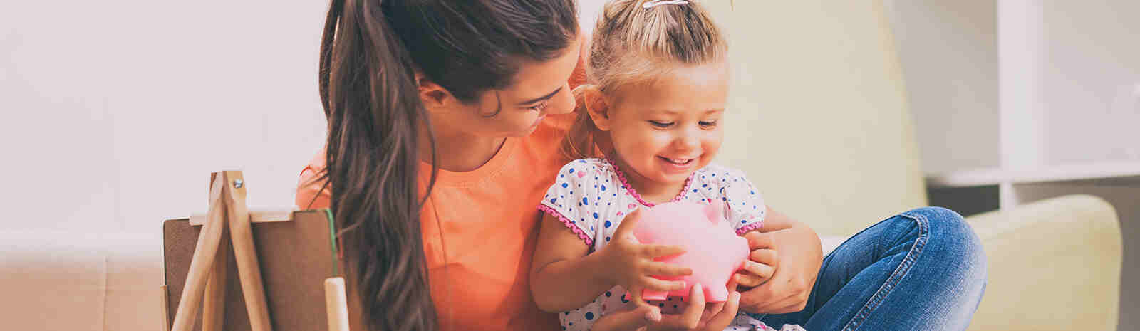 Happy young mom holds daughter and piggy bank.