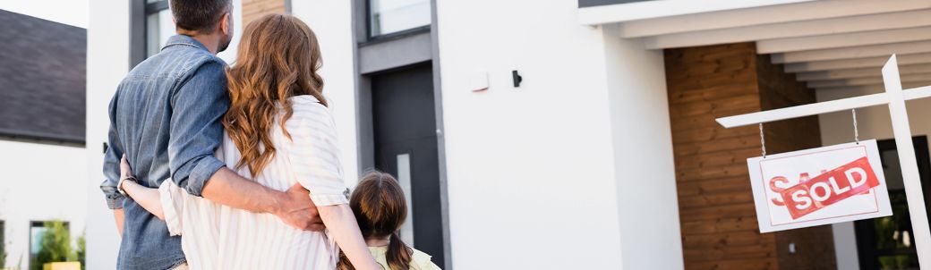 Young family standing in front of sold sign for their home.