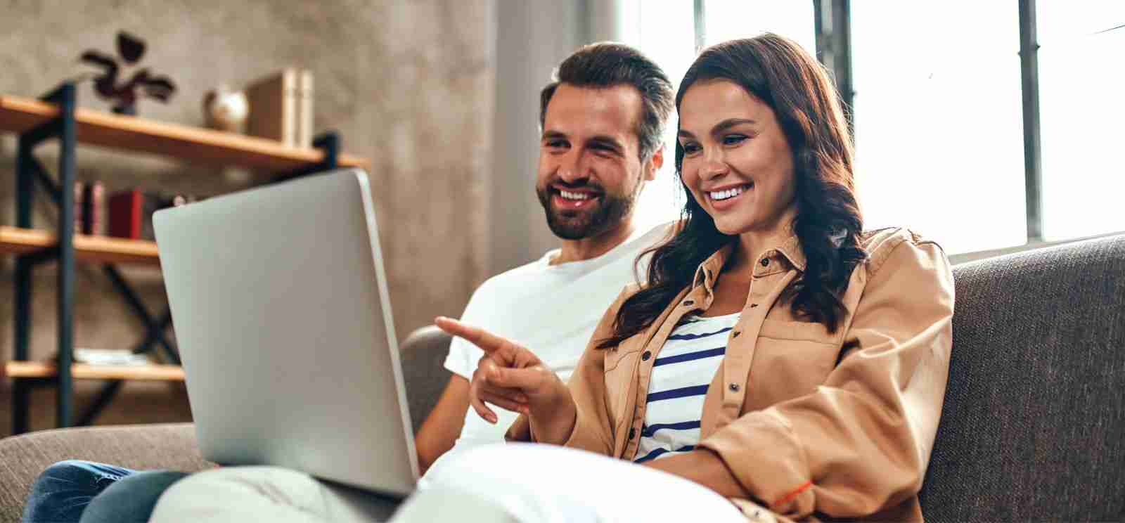 Man and woman sitting on a couch at home looking at a shared laptop