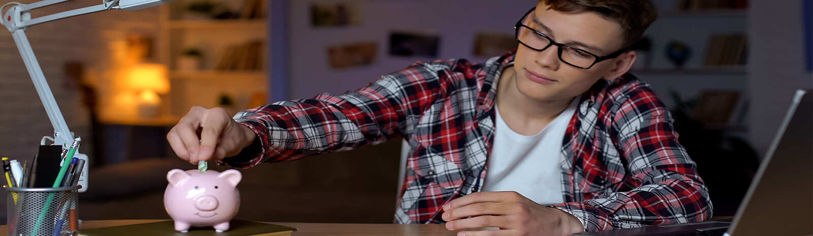 Middle school aged kid in his bedroom puts money in his piggy bank.