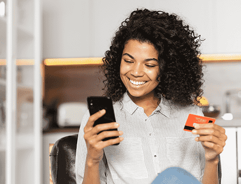 Woman looking at phone in left hand smiling and holding debit card in right hand