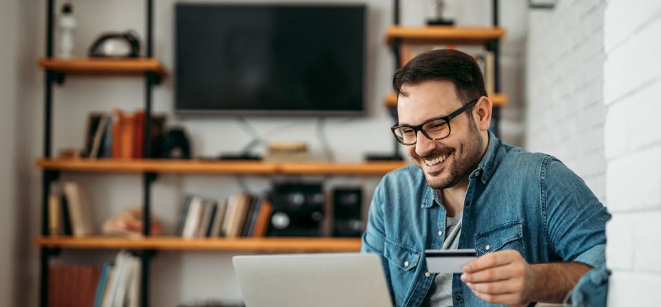 man smiling while using his laptop and holding credit card